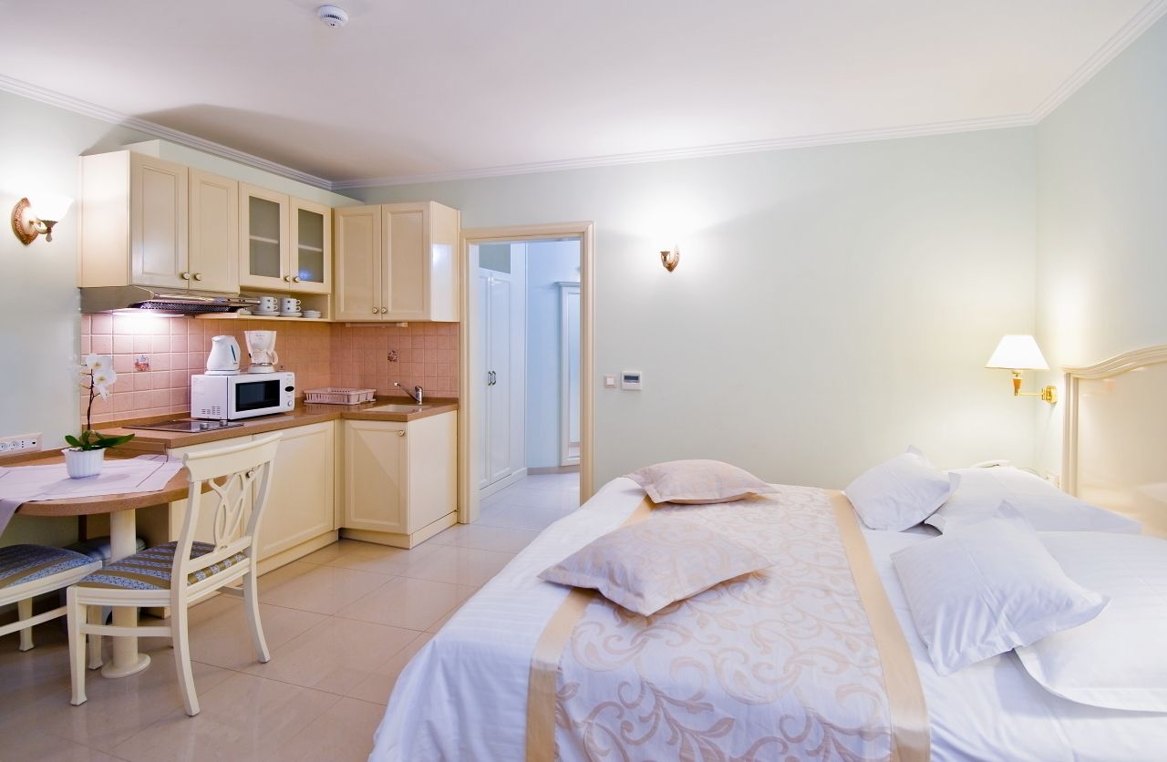Habitación de hotel compacta con kitchenette, zona de comedor y cama con cabecero decorativo.