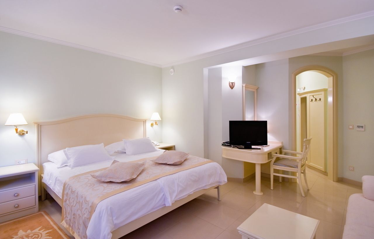 A hotel room with a bed, bedside tables, a desk with a TV, and a chair.