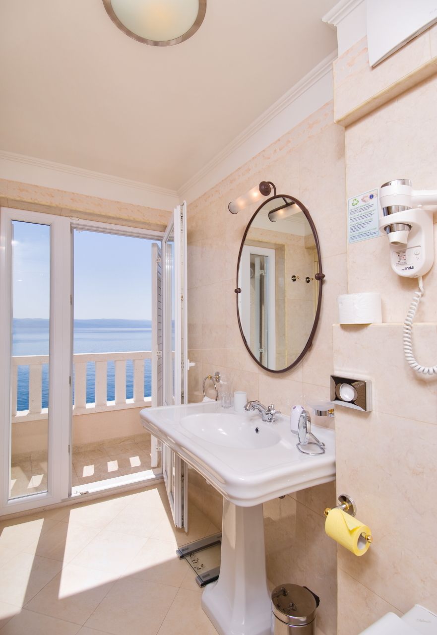 A bathroom with a sink, mirror, and hairdryer, with a view of the sea through the door.