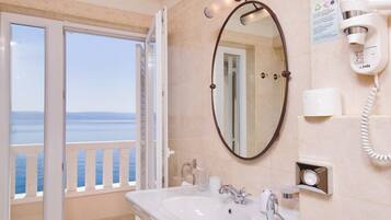A bathroom with a sink, mirror, and hairdryer, with a view of the sea through the door.