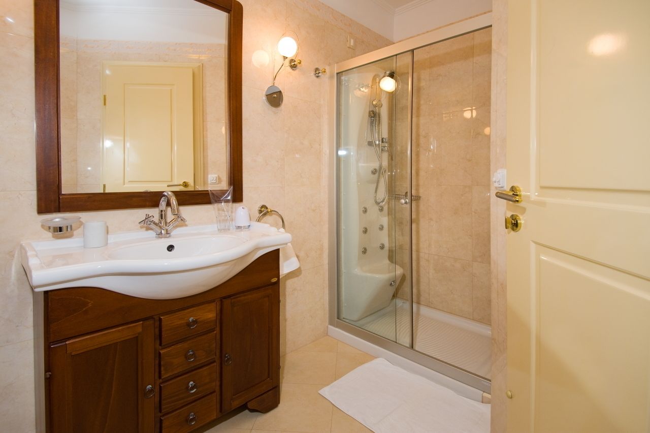 Une salle de bain avec un lavabo blanc, un meuble-lavabo en bois, un grand miroir et une douche à parois de verre.