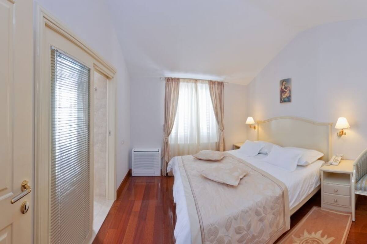 A hotel room with a bed, bedside table, lamp, chair, and a window with curtains.