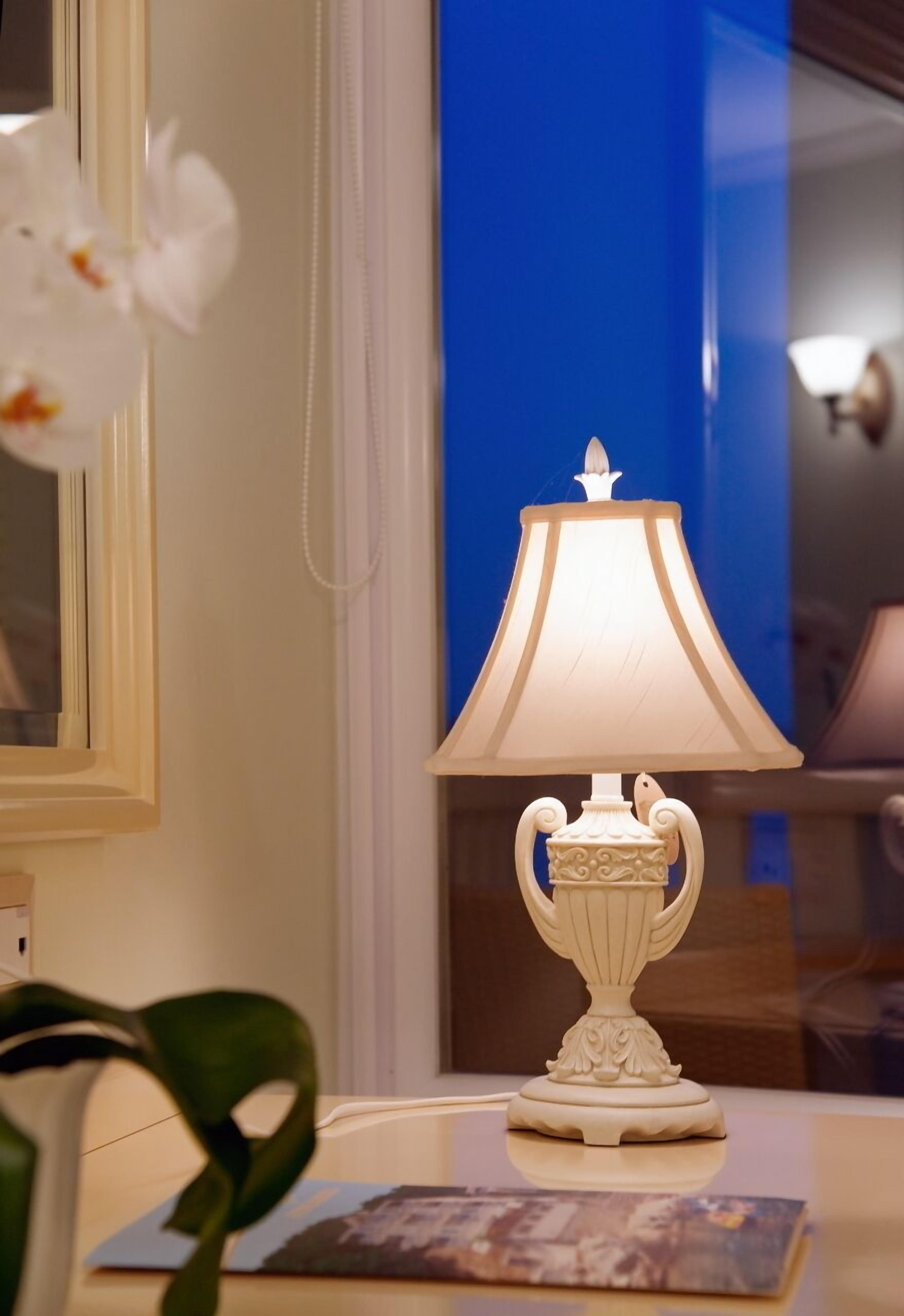 Une lampe de table avec un abat-jour blanc et un pied décoratif, posée sur une table sur laquelle se trouve un tableau encadré.