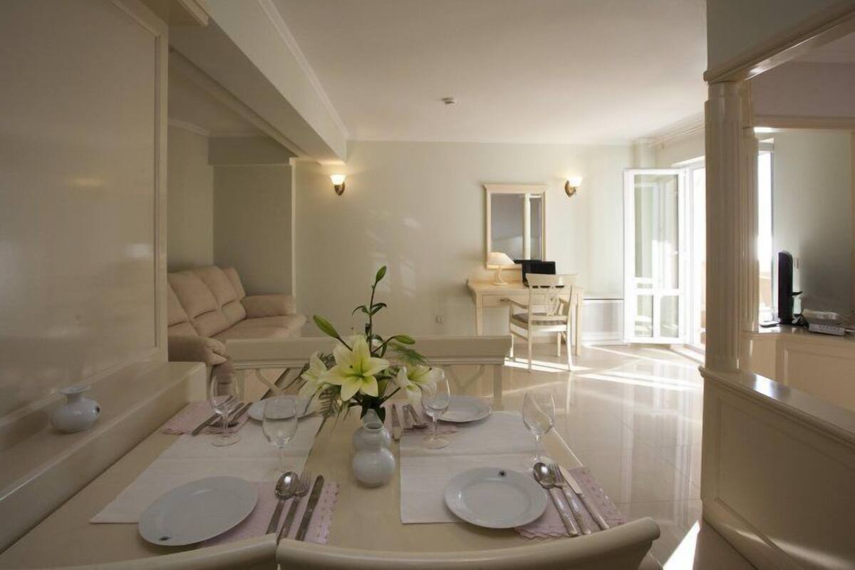 A dining area with a table set for four, a sofa, and a small side table with a vase of flowers.