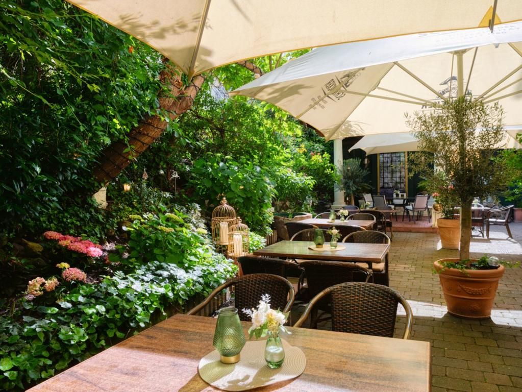 Un área de comedor al aire libre con mesas y sillas, rodeada de abundante follaje y plantas en macetas.