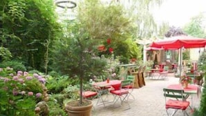 Een terras buiten met tafels en stoelen, omgeven door weelderige beplanting en bloempotten.