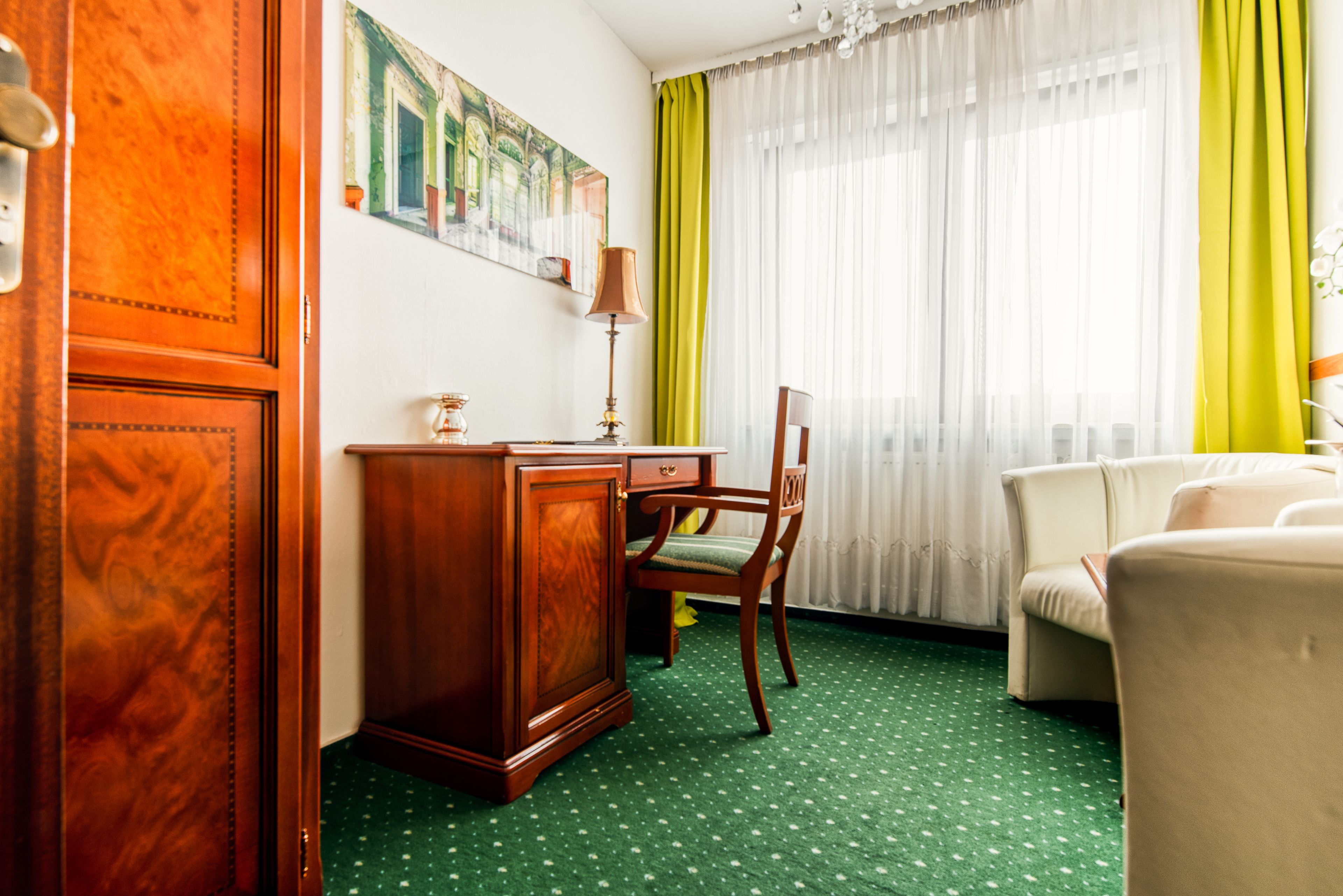 Una habitación con un escritorio de madera, una silla, un sofá y un ventanal con cortinas amarillas.