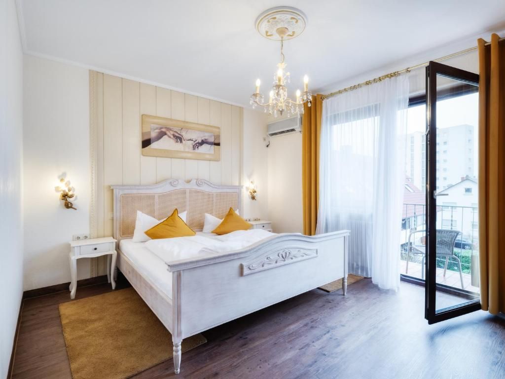 A hotel room with a bed, bedside tables, a chandelier, a window with curtains, and a view of the outside.