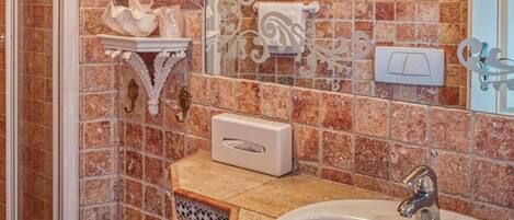 Un baño con un lavamanos grande, azulejos decorativos en la pared, un espejo y una zona de ducha.