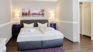 Une chambre d’hôtel avec un grand lit, deux tables de chevet, un tableau représentant un paysage urbain accroché au mur et un tapis violet.