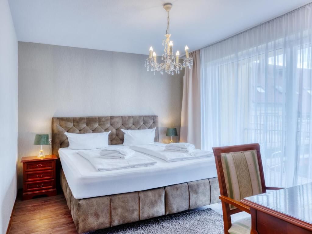 Ein Hotelzimmer mit einem großen Bett, einem Kronleuchter, einem Nachttisch, einem Sessel und einem Fenster mit Vorhängen.