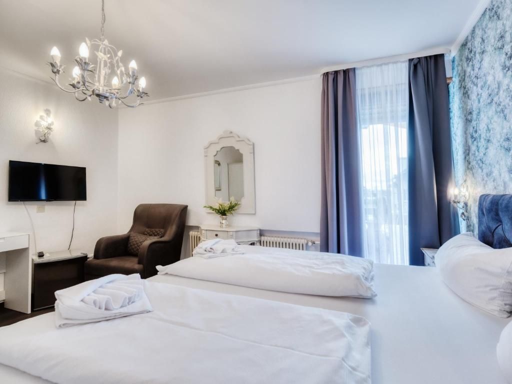 Ein Hotelzimmer mit zwei Betten, einem Fernseher, einem Sessel und einer Kristallleuchtre.