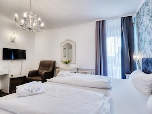 A hotel room with two beds, a TV, a chair, and a chandelier.
