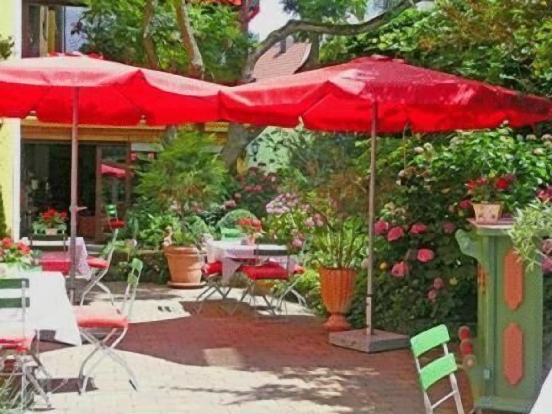 An outdoor patio area with red umbrellas, potted plants, and outdoor seating.