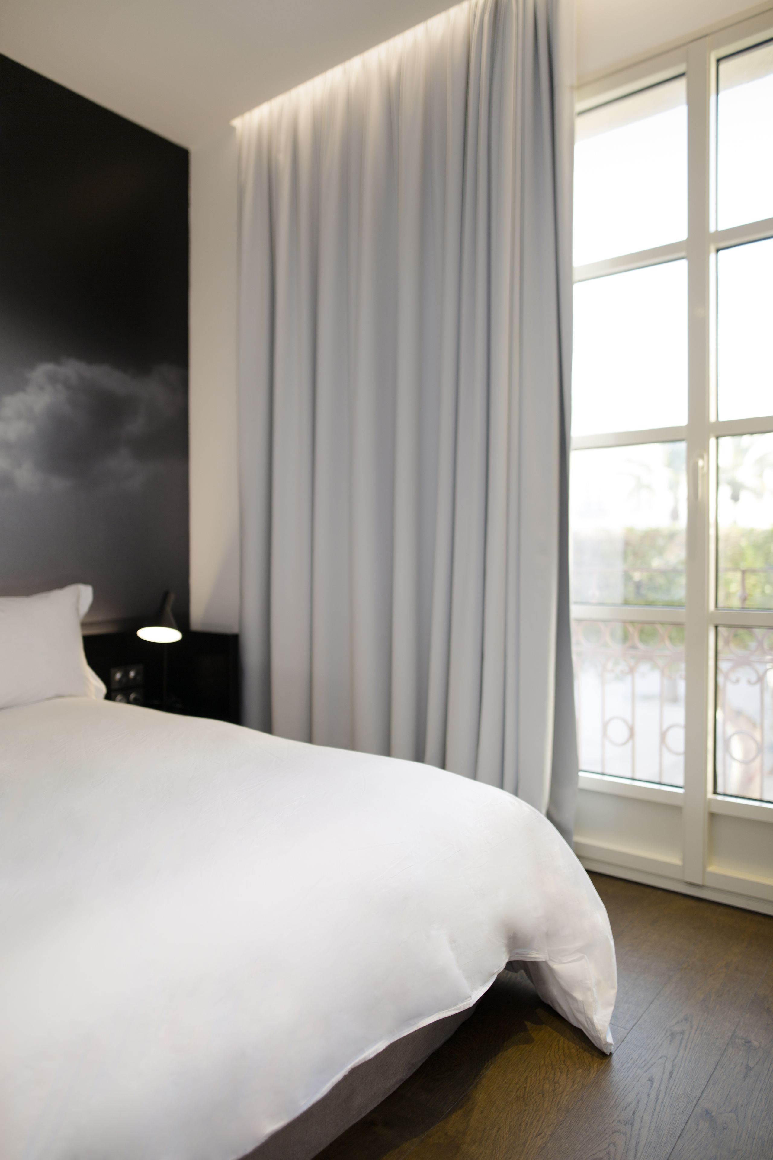 Un dormitorio moderno con una cama grande, una mesita de noche, una lámpara y una ventana con cortinas.
