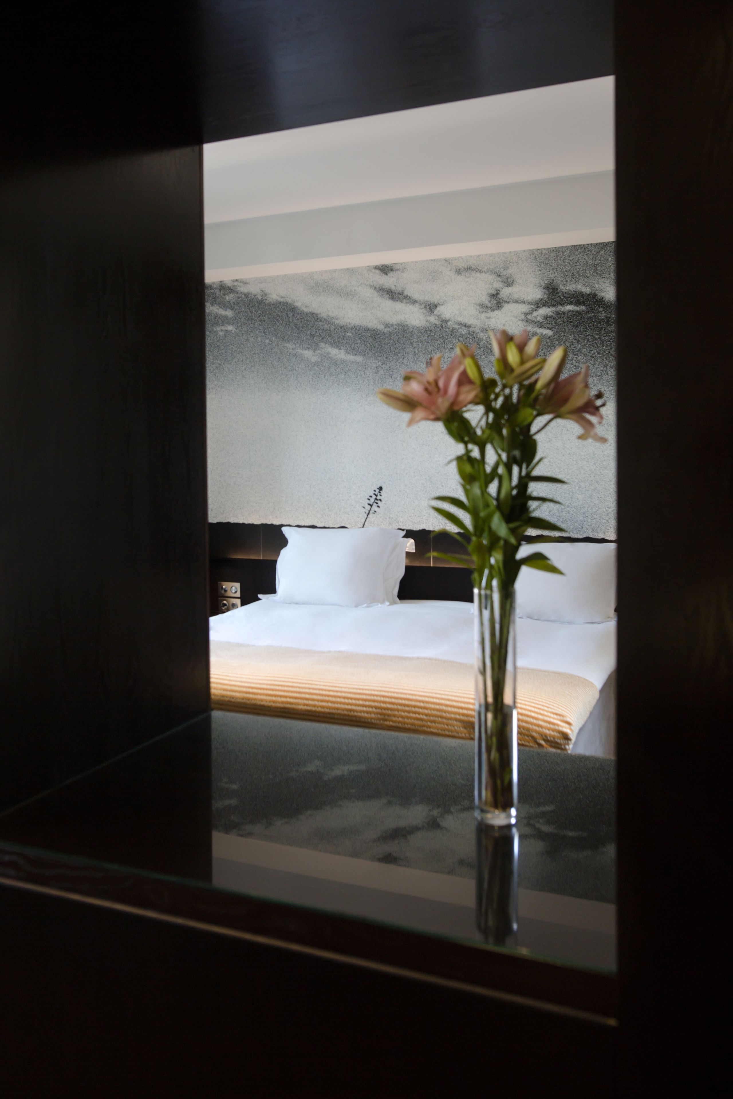 Una habitación de hotel moderna con una cama grande, una mesita de noche y un jarrón con flores.