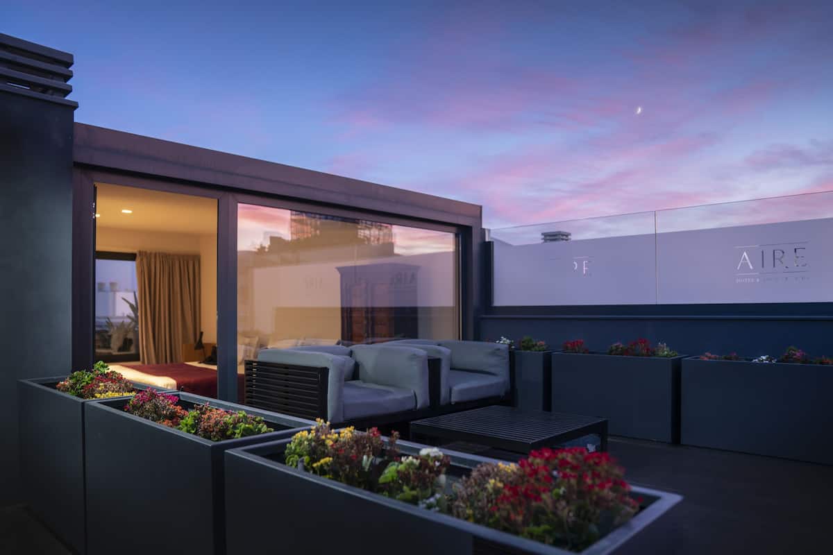 A modern outdoor seating area with a sofa and a table, surrounded by flower planters.