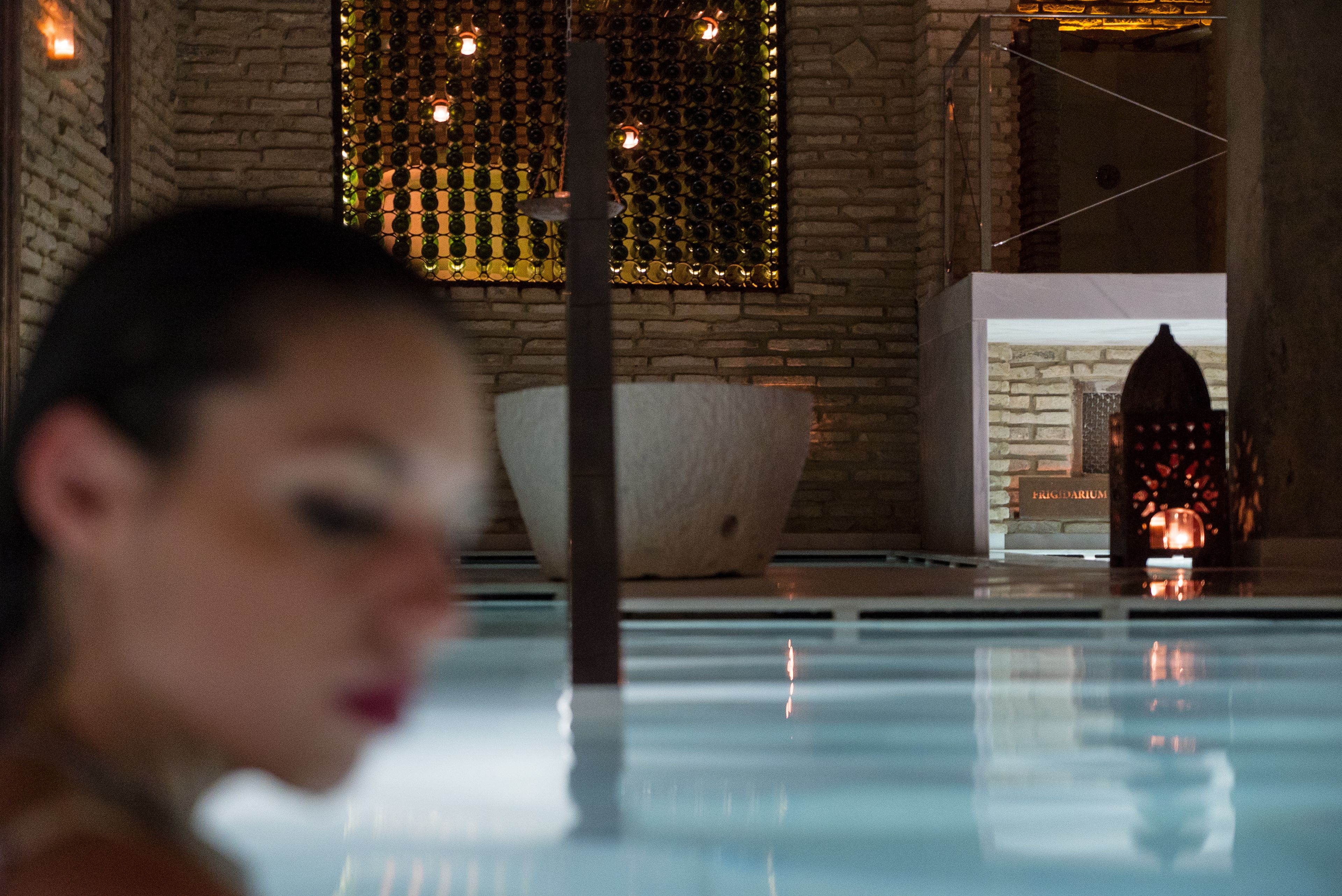 Un espacio de spa con pared de piedra, un recipiente blanco grande y un farol decorativo.
