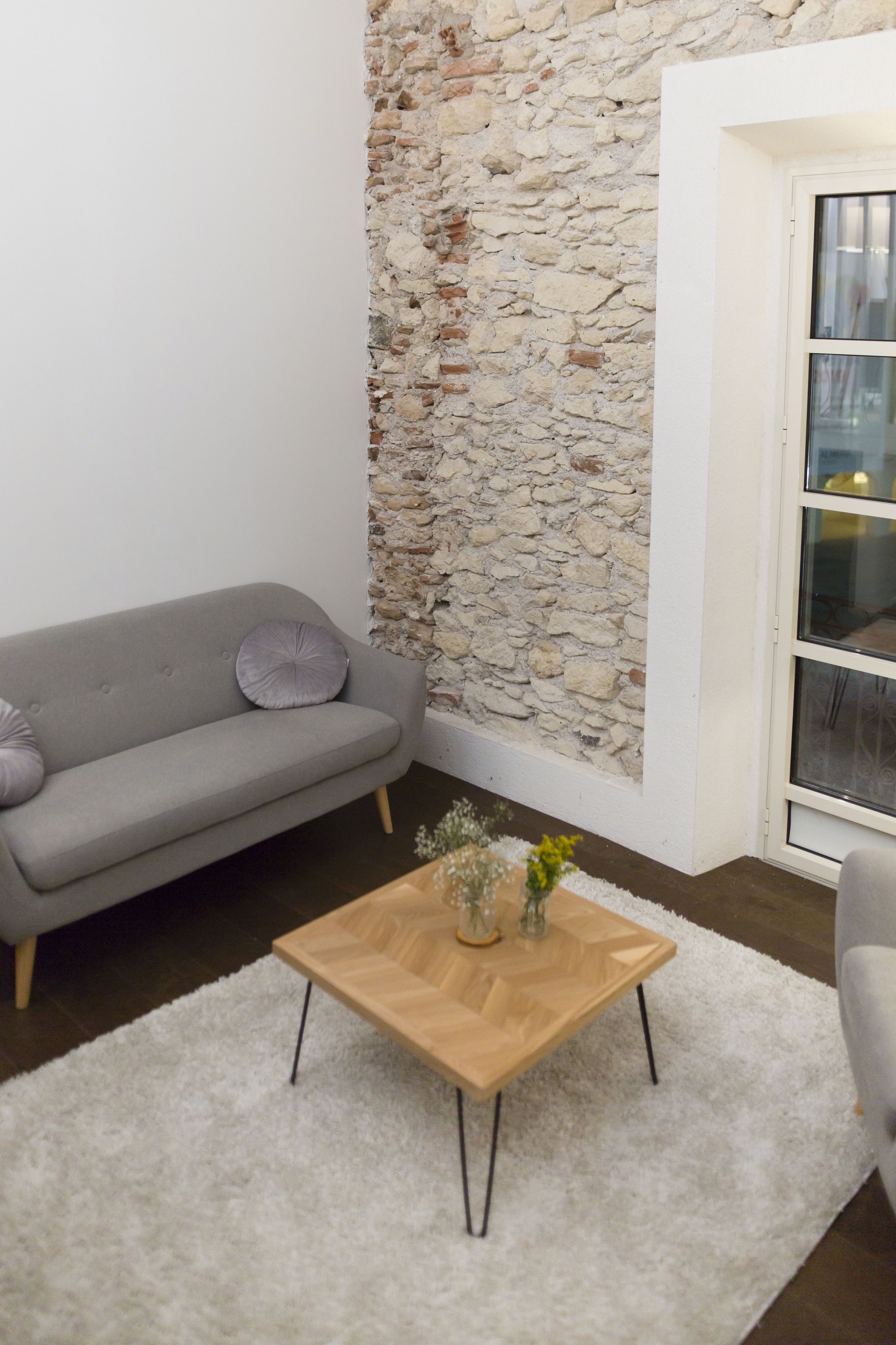 Una sala de estar con un sofá gris, una mesa de centro de madera, un tapete blanco y mullido, y una pared de piedra.