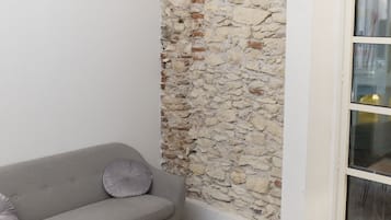 Una sala de estar con un sofá gris, una mesa de centro de madera, un tapete blanco y mullido, y una pared de piedra.