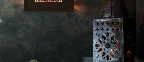 A dark textured wall with a sign labeled "BALNEUM" and a decorative metal object with a glass top.
