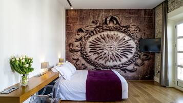 Un dormitorio moderno con un mural grande en la pared, un escritorio de madera, una cama con un plaid morado y un televisor en la pared.