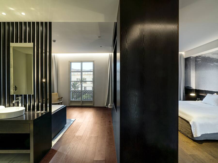 A modern hotel room with a large bed, a bathroom with a vanity, and a view of the city through the window.