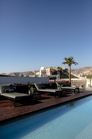 Zona de piscina en la azotea con sillones y vista a un edificio histórico.
