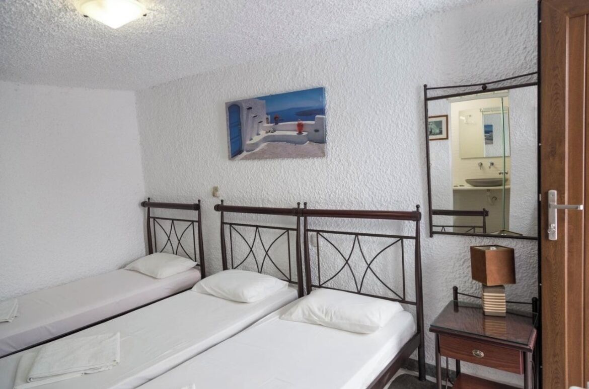 Une chambre avec deux lits simples, une tête de lit en bois, un tableau, un miroir et une table de chevet avec une lampe.