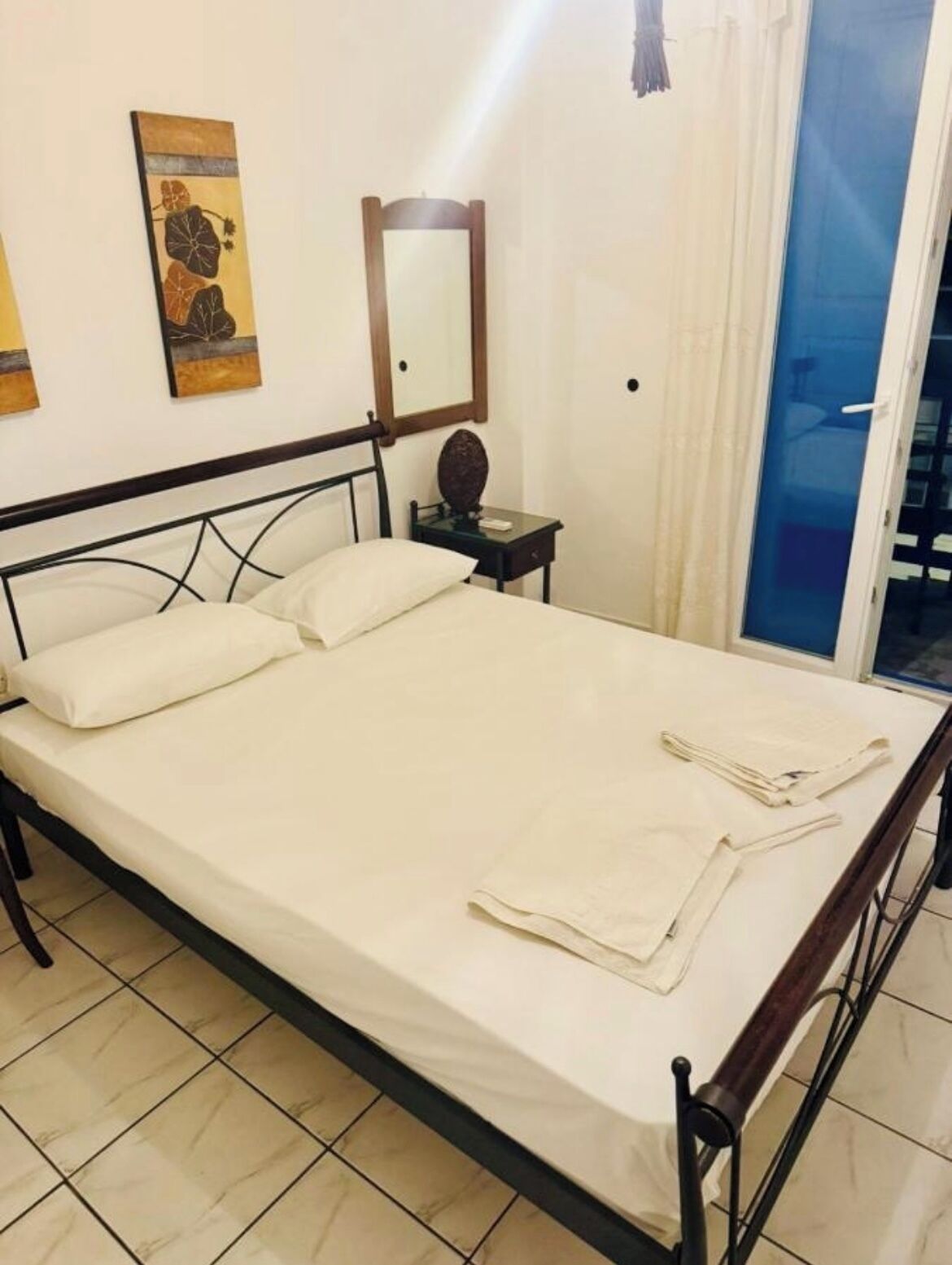 A single bed with a wooden frame, a bedside table with a lamp, and a mirror on the wall.