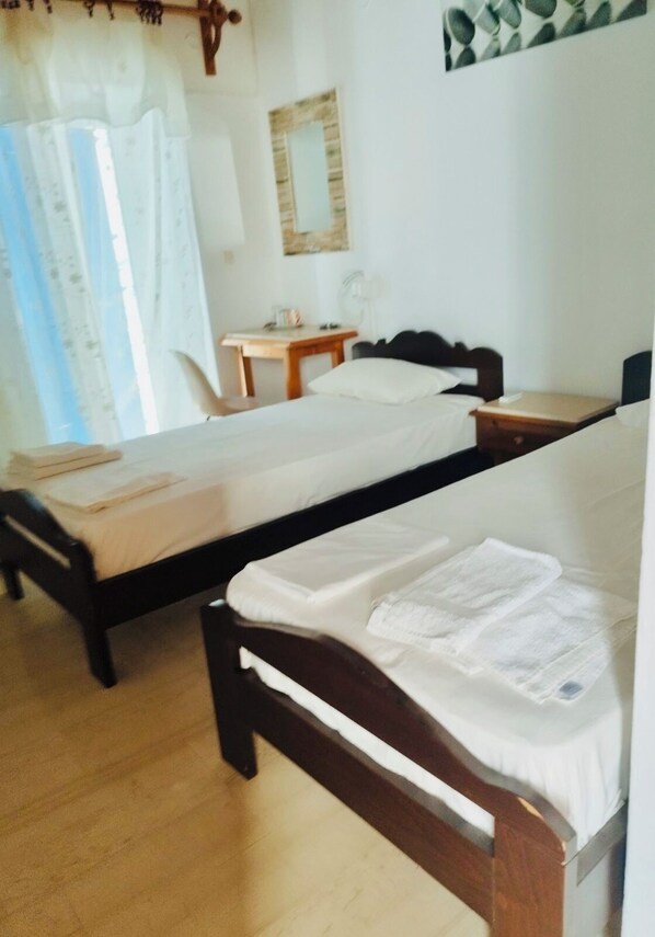 A room with two wooden beds, a small wooden table, a chair, a mirror, and a window with curtains.