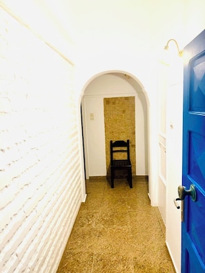 En smal hall med en vit tegelvägg, en blå dörr och en stol i mitten.