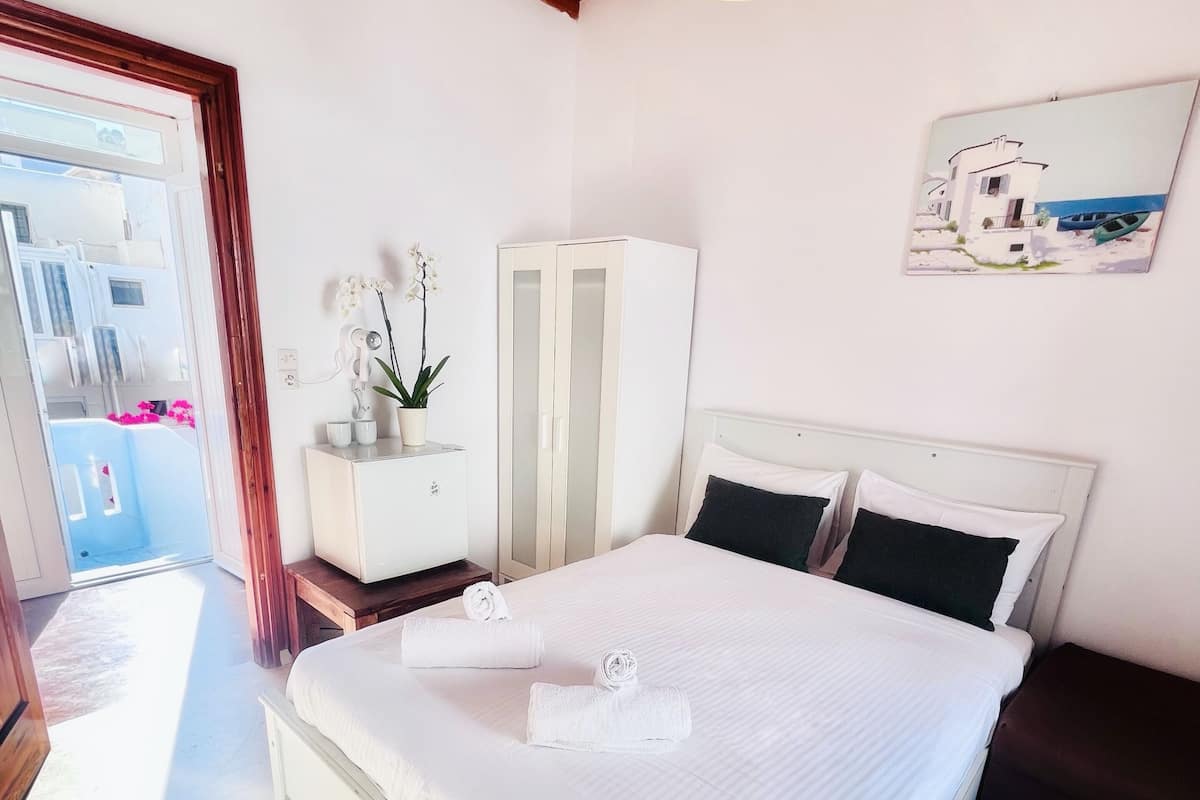 A bedroom with a bed, a wardrobe, a desk with a plant, and a painting on the wall.