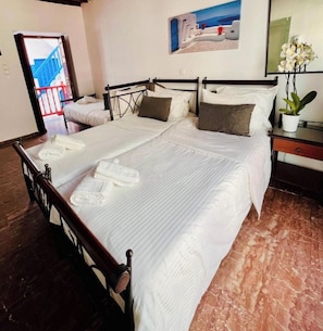 A double bed with white linens, a wooden headboard, a nightstand with a plant, and a painting of a coastal scene. - Studio Eleni (Mykonos)