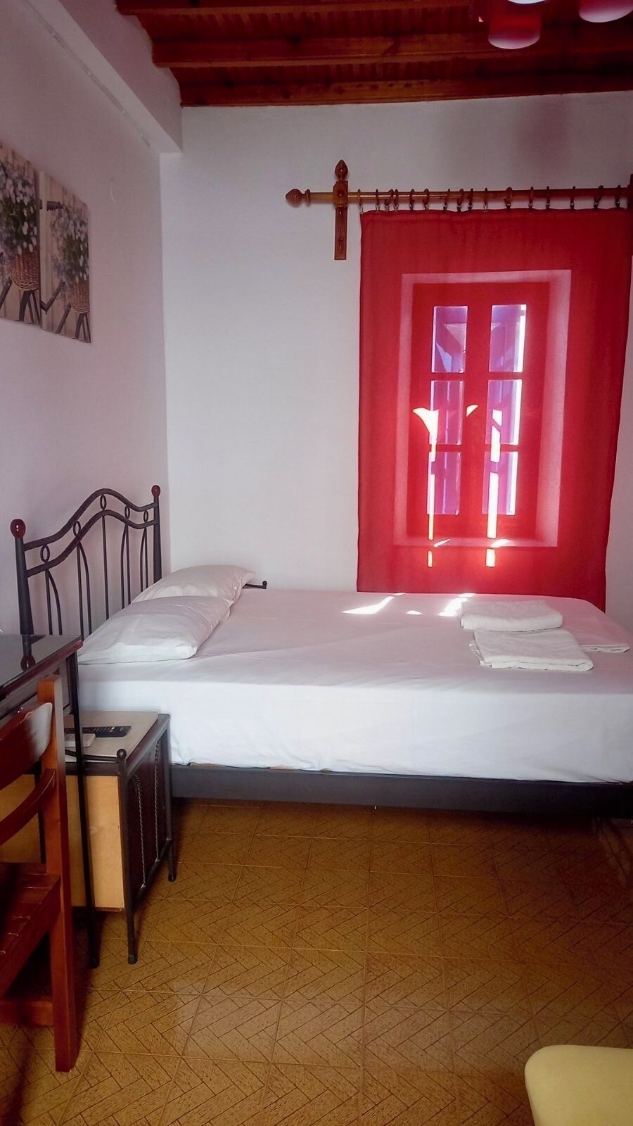 Une pièce comprenant un lit, un bureau, une chaise, une fenêtre avec un rideau rouge et un plancher en bois.