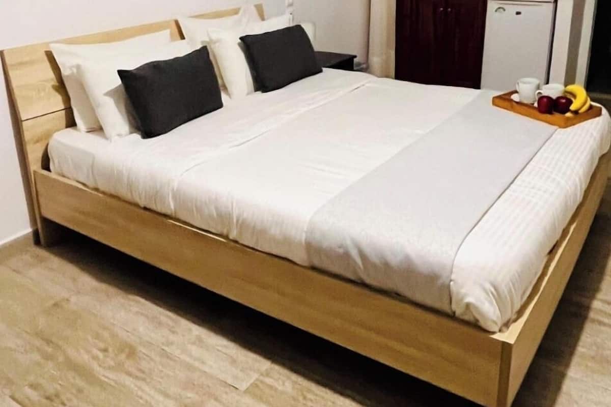 A bed with a wooden frame, white bedding, and a tray with fruits and cups.