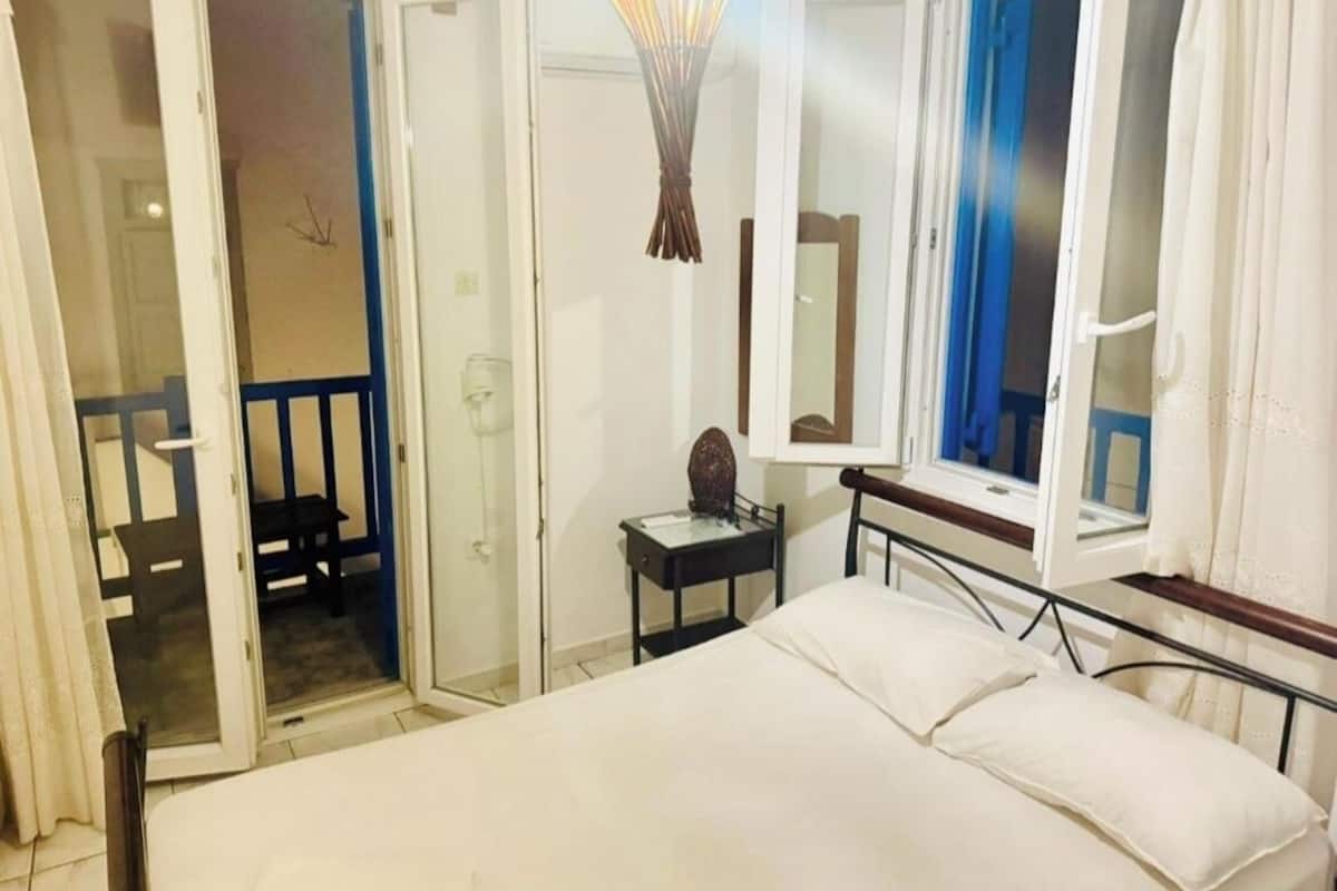 A bedroom with a bed, a bedside table, a mirror, and a window with curtains.