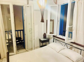 Une chambre à coucher avec un lit, une table de chevet, un miroir et une fenêtre avec des rideaux.