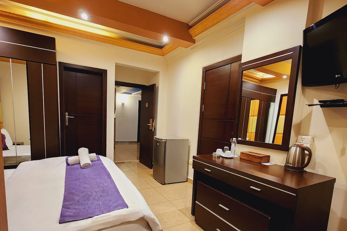 Una habitación de hotel con una cama, un aparador, un espejo, un televisor y un refrigerador.