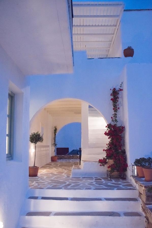 A white building with a stone-paved entrance and a covered area with arches.