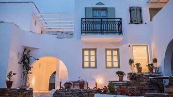 A white building with a balcony, potted plants, and an archway.