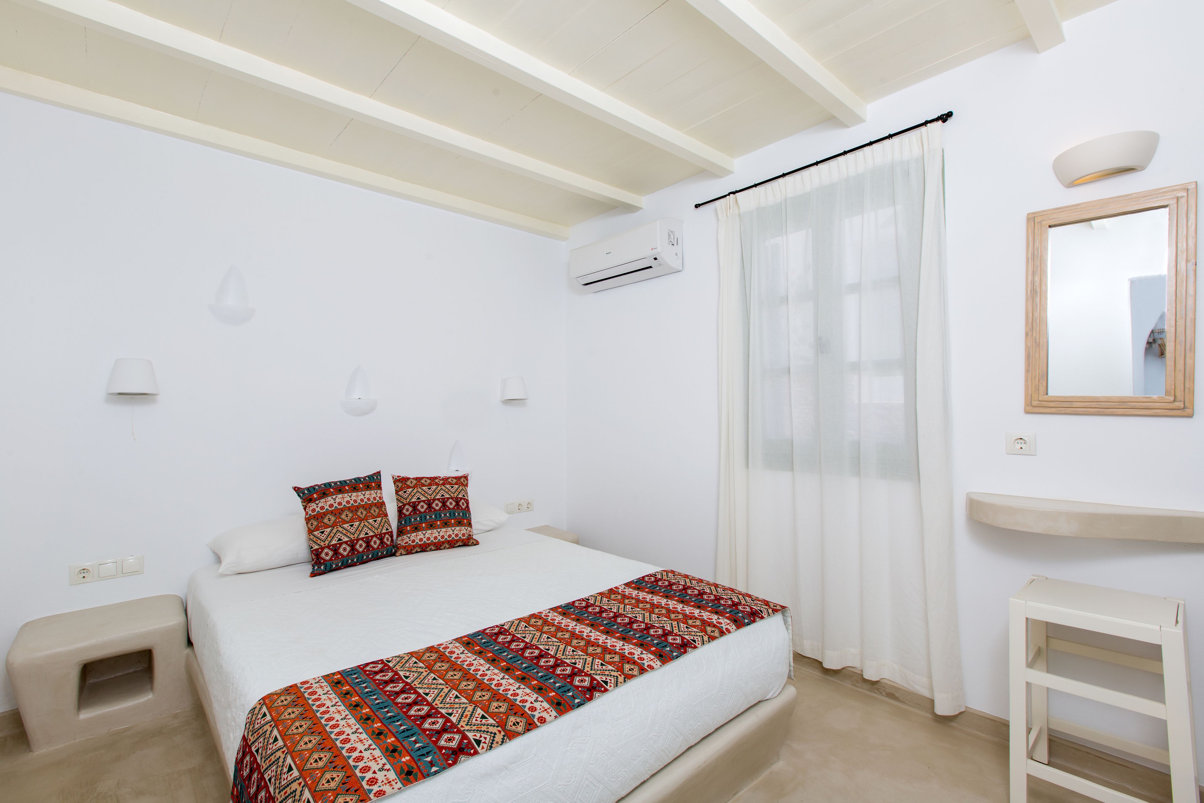 A bedroom with a bed, a bedside table, a mirror, and an air conditioning unit.