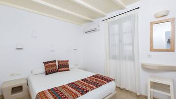 A bedroom with a bed, a bedside table, a mirror, and an air conditioning unit.