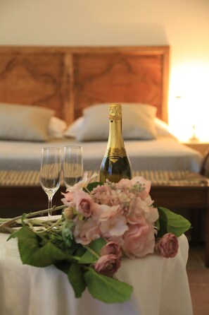 A bed with pillows and a bedside table with a bottle of champagne, two glasses, and a floral arrangement. - La Corte delle 4 Stagioni (Ozzano Monferrato)
