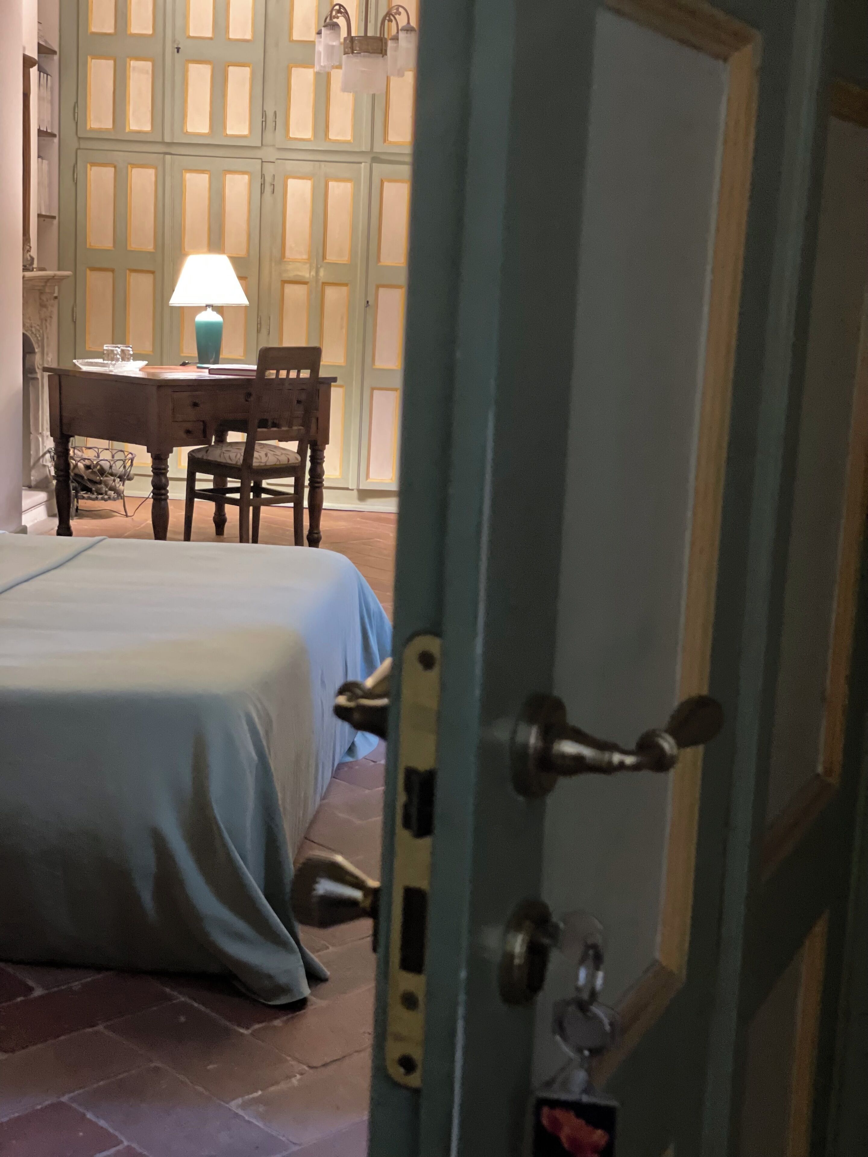 A room with a bed, a desk, and a chair. There is a door with a lock and a keyhole.