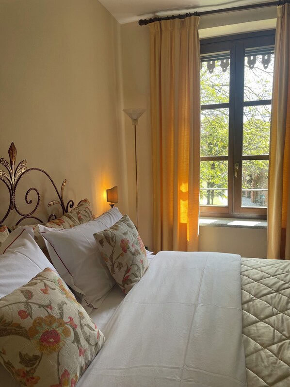 A hotel room with a bed, floral pillows, a floor lamp, and a window with curtains.