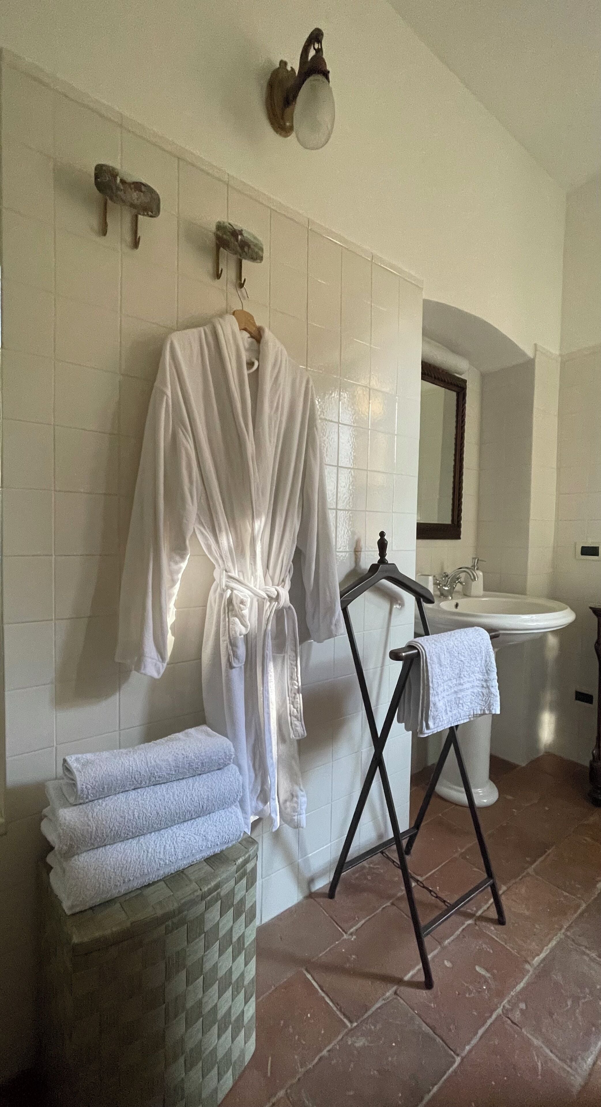 Un baño con una bata blanca colgada en la pared, un lavamanos y un espejo.
