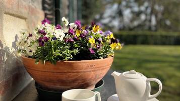 A terracotta flower pot with a variety of flowers on a balcony table, accompanied by a white teapot and cup.