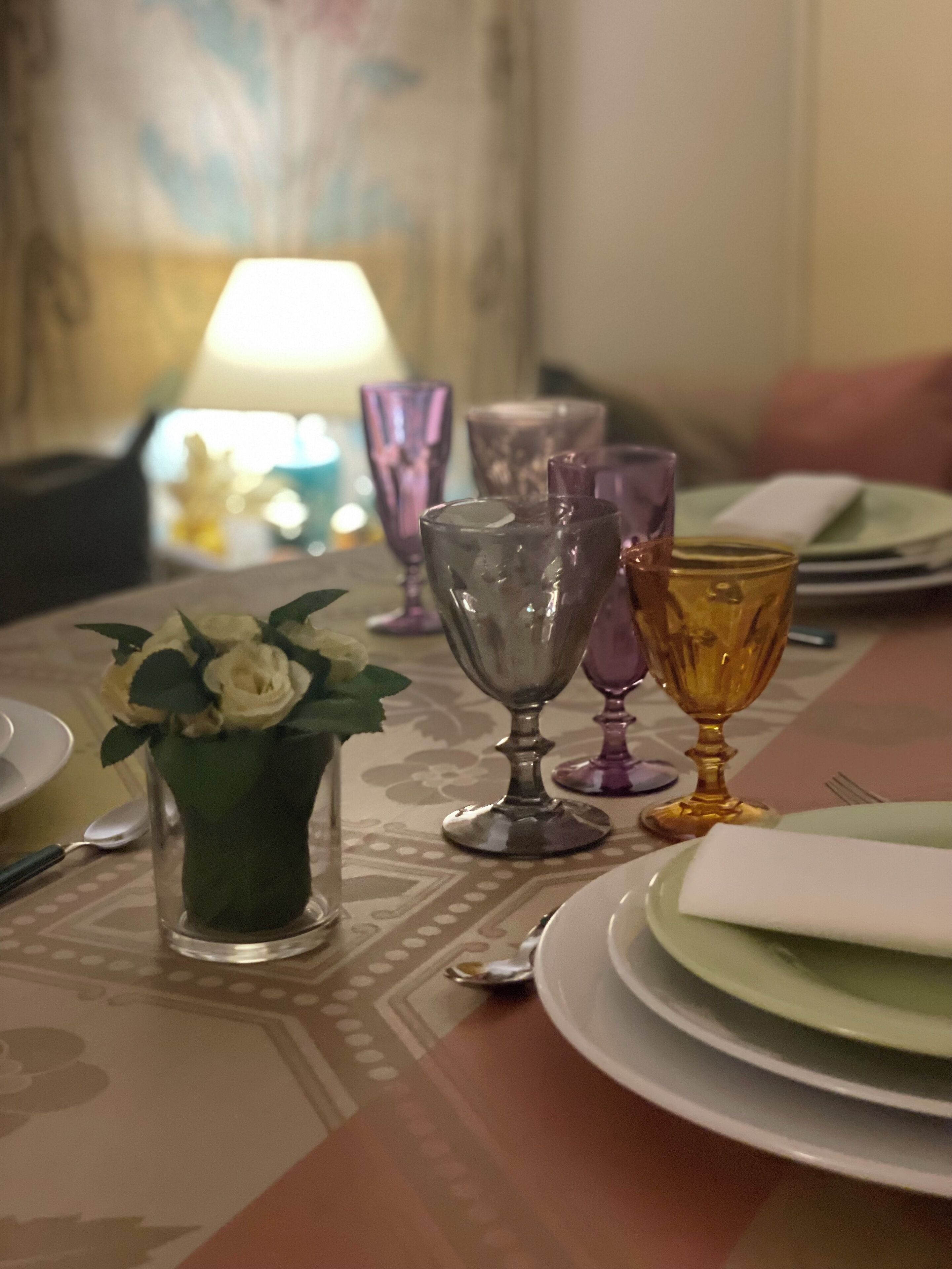 Une table à manger ornée d’un vase de fleurs blanches, de plusieurs verres à vin et d’assiettes.