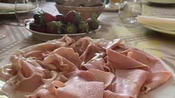 Una mesa de comedor con un plato de jamón en rodajas, un bol de fresas y un vaso de agua.